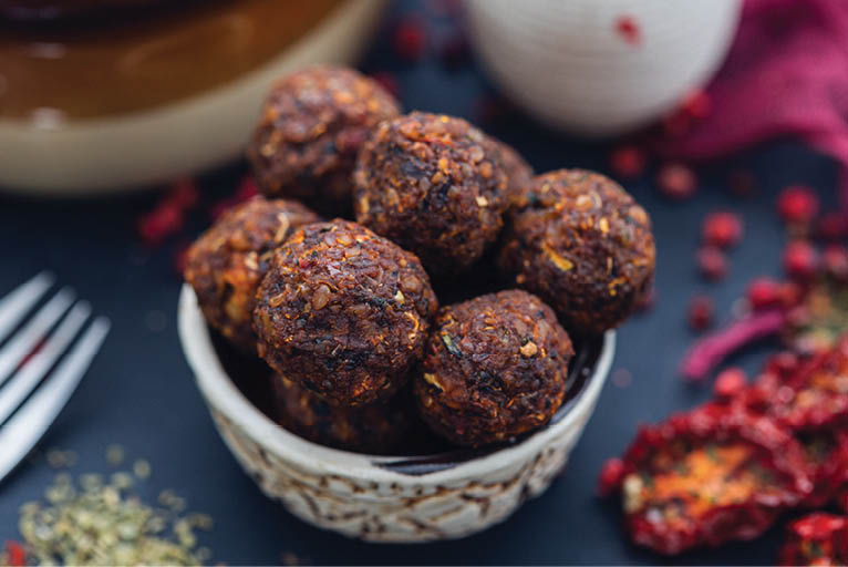 Bowl of raw vegan meat balls surrounded with vegetables on a dark tabletop flat lay  Veggie meatballs  