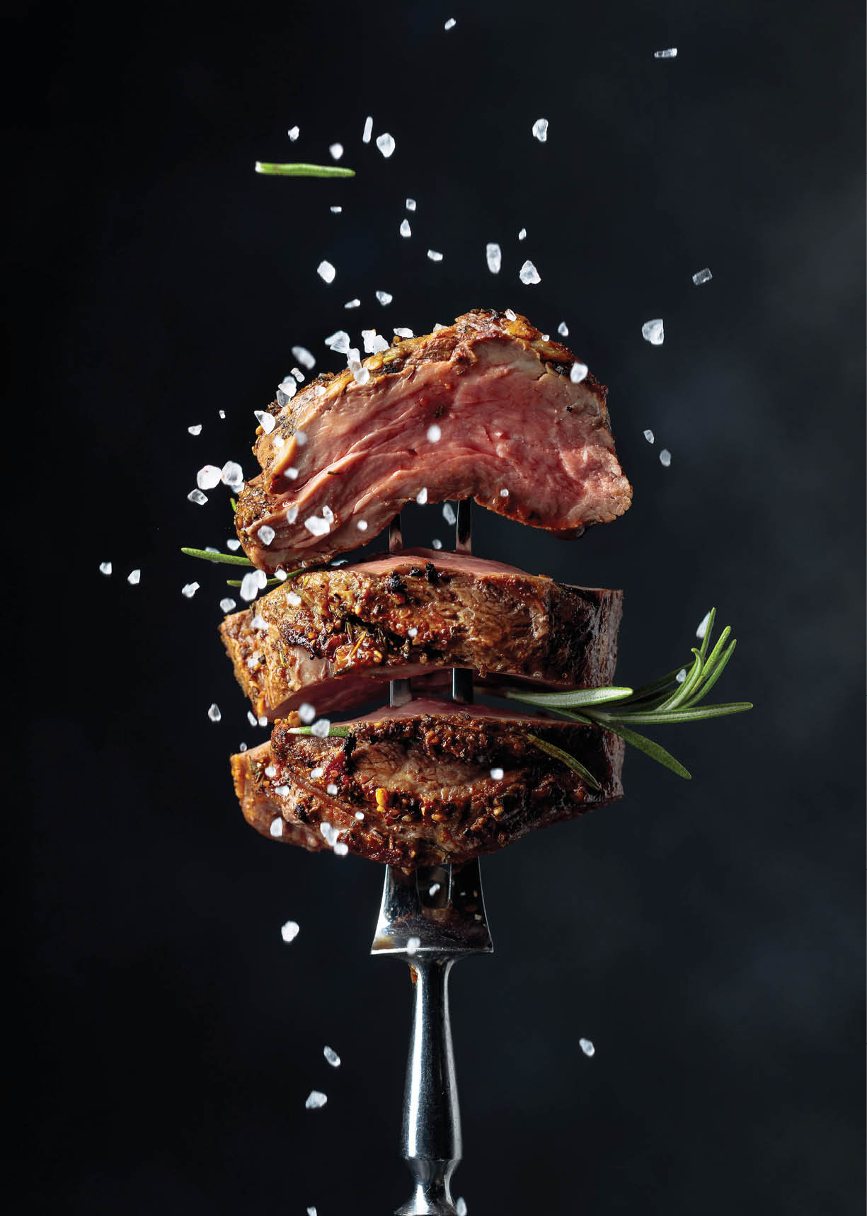 Grilled beef steak with spices on a black background. Beef steak on a fork sprinkled with rosemary and sea salt.  