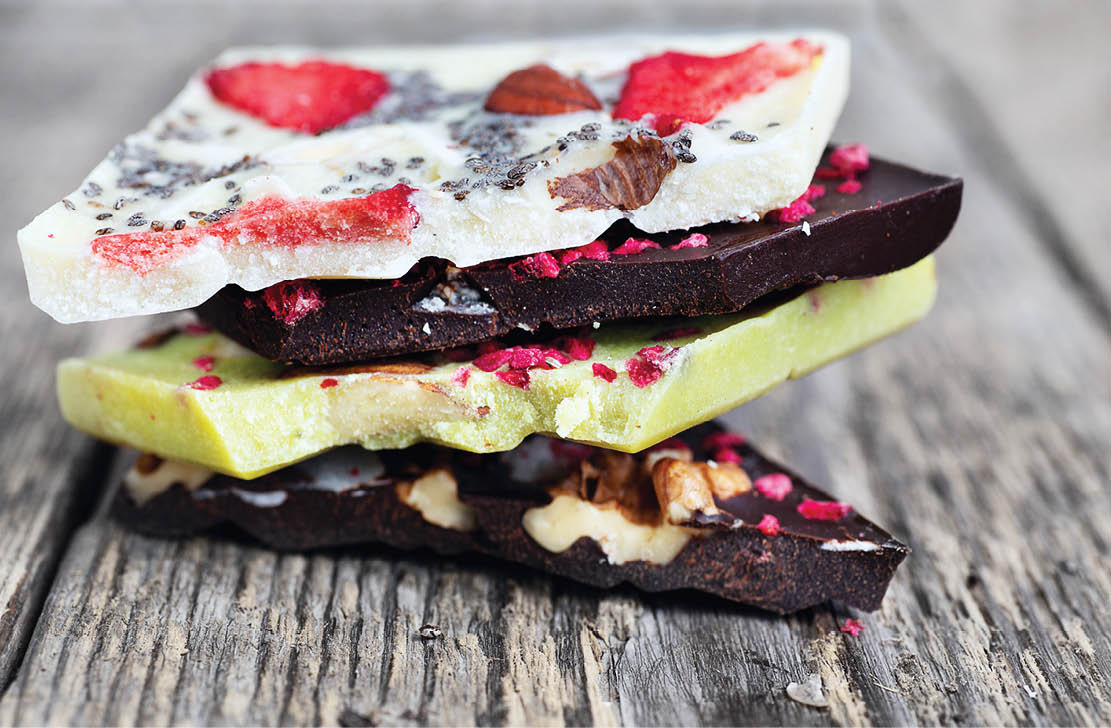 Bars of chocolate with sublimated berries, nuts and seeds on the wooden board. Raw vegan chocolate. Lactose free chocolate. Gluten free chocolate. Without artificial dyes.