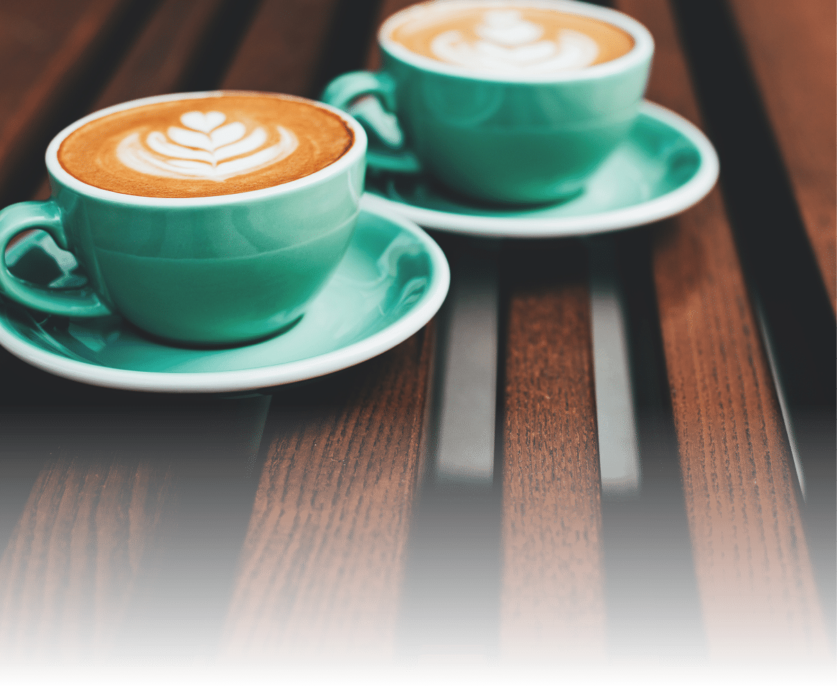 Two cups of cappuccino with latte art on wooden background. Beautiful foam, greenery ceramic cups, stylish toning, place for text.