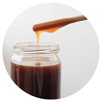 frontal image of glass jar with screw cap containing barley or rice malt with casting of product from a stick or wooden spoon - excellent natural sweetener on gradient white back