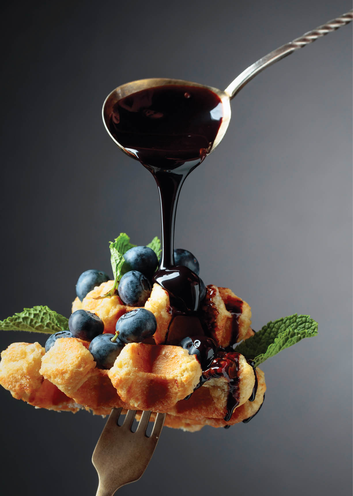 Belgian waffles with chocolate syrup, blueberry and mint on a dark background. 