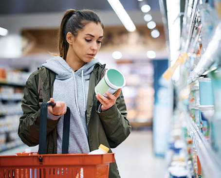 Young woman buying diary product and reading food label in grocery store.