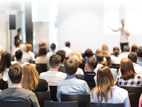 Speaker giving a talk in conference hall at business event. Audience at the conference hall. Business and Entrepreneurship concept. Focus on unrecognizable people in audience.