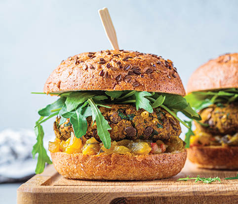 Vegan lentil burger with arugula, mustard sauce, fresh vegetables and sweet potato fries on a wooden board. Vegan food concept.
