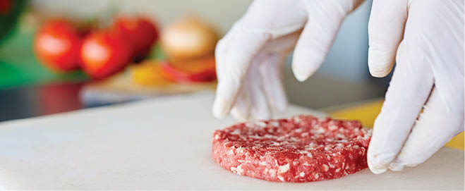 Cropped image of hands wearing white latex gloves preparing a hamburger patty in a clean and hygeinic environment 
