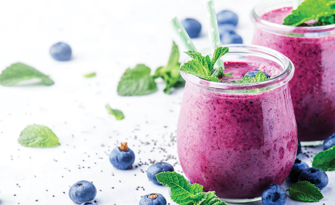 Purple homemade yogurt or smoothie with blueberries, chia seeds and mint leaves in glass jars on gray background, selective focus