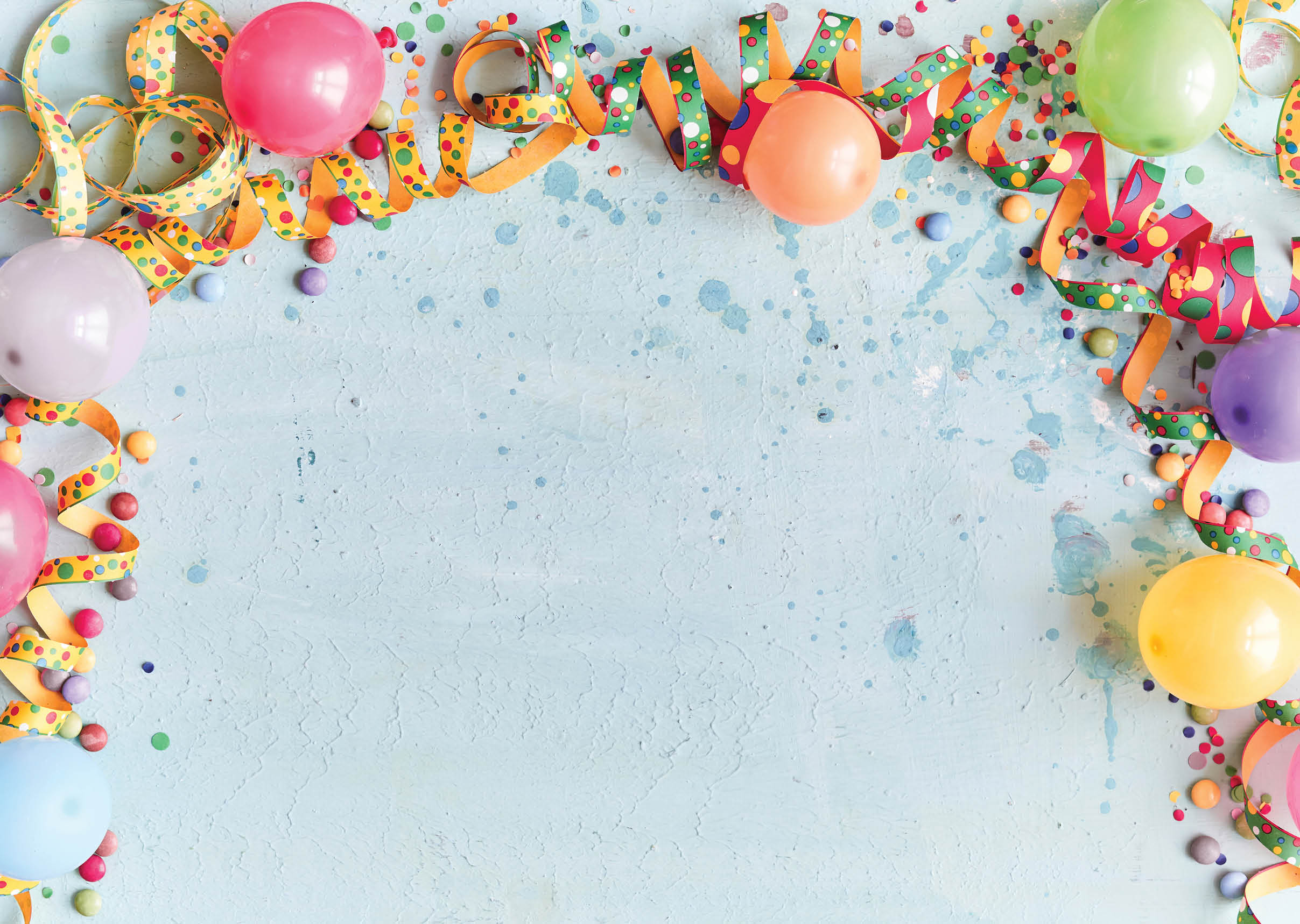 Carnival, festival or birthday balloon background with colorful party streamers, candy and confetti making a border on a blue background with copy space